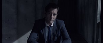Movie still from “Anon” (2018), directed by Andrew Niccol – A man wearing a suit and tie sitting in a dark room; Close Up shot, Over the shoulder angle