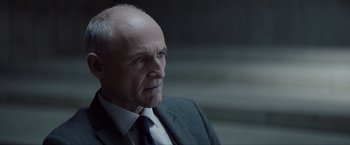 Movie still from “Anon” (2018), directed by Andrew Niccol – An older man wearing a suit and tie; Close Up shot, Over the shoulder angle