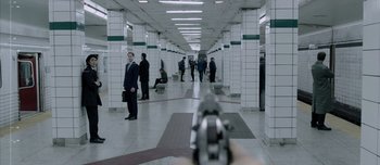 Movie still from “Anon” (2018), directed by Andrew Niccol – A gun pointed at a group of people in a hallway; Wide shot, High angle