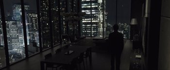 Movie still from “Anon” (2018), directed by Andrew Niccol – A man standing in front of a large window at night; Wide shot, High angle