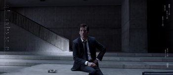 Movie still from “Anon” (2018), directed by Andrew Niccol – A man in a suit and tie sitting on the ground; Wide shot, Low angle