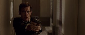 Movie still from “Anon” (2018), directed by Andrew Niccol – A man holding a gun while wearing a suit and tie; Close Up shot, Low angle