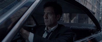 Movie still from “Anon” (2018), directed by Andrew Niccol – A person sitting in a car wearing a suit; Close Up shot, Low angle