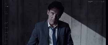Movie still from “Anon” (2018), directed by Andrew Niccol – A man wearing a suit and tie standing in front of a wall; Close Up shot, Low angle