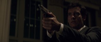 Movie still from “Anon” (2018), directed by Andrew Niccol – A man holding a gun while wearing a suit and tie; Close Up shot, Low angle