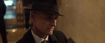 Movie still from “Anon” (2018), directed by Andrew Niccol – A person wearing a suit and a hat; Close Up shot, Over the shoulder angle