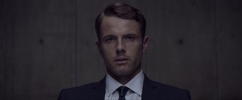 Movie still from “Anon” (2018), directed by Andrew Niccol – A person wearing a suit and tie; Close Up shot, Over the shoulder angle