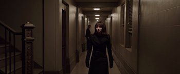 Movie still from “Anon” (2018), directed by Andrew Niccol – A woman in a black coat walking down a hall way; Medium shot, Over the shoulder angle