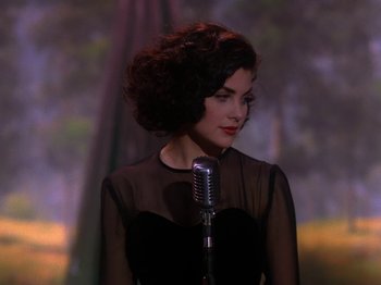 Movie still from “Twin Peaks” (1990), created by David Lynch – A woman in a black dress holding a microphone; Close Up shot, Over the shoulder angle