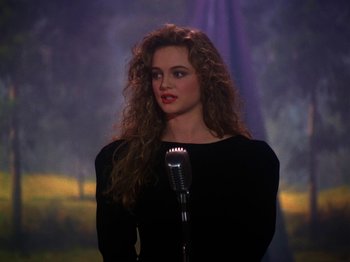 Movie still from “Twin Peaks” (1990), created by David Lynch – A woman with long curly hair is holding a microphone; Close Up shot, Over the shoulder angle