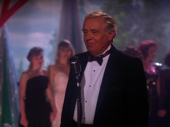 Movie still from “Twin Peaks” (1990), created by David Lynch – An older man in a tuxedo is holding a microphone; Medium shot, Over the shoulder angle