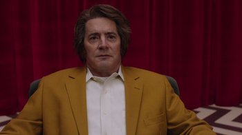 Movie still from “Twin Peaks” (2017), directed by David Lynch – A man in a yellow jacket sitting in a chair in front of a red curtain; Close Up shot, Low angle
