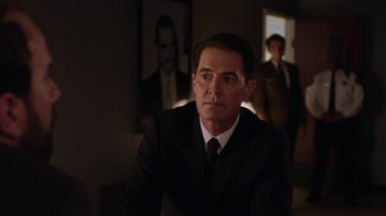 Movie still from “Twin Peaks” (2017), directed by David Lynch – A man wearing a suit and tie in a room; Medium shot, Over the shoulder angle