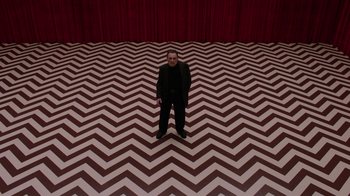 Movie still from “Twin Peaks” (2017), directed by David Lynch – A man standing in a room that has red walls and a black and white floor; Wide shot, High angle