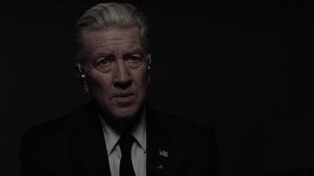 Movie still from “Twin Peaks” (2017), directed by David Lynch – A person wearing a suit and ear buds; Close Up shot, Over the shoulder angle