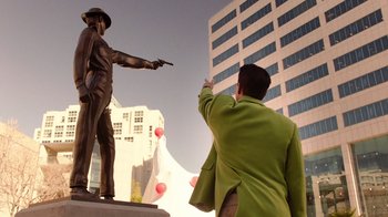 Movie still from “Twin Peaks” (2017), directed by David Lynch – A man pointing to a statue of a man in a green jacket; Medium shot, Over the shoulder angle