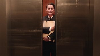Movie still from “Twin Peaks” (2017), directed by David Lynch – A man in a suit and tie standing in an elevator holding a clipboard; Medium shot, Low angle
