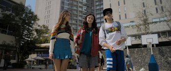 Movie still from “Anonymously Yours” (2021), directed by Maria Torres – A group of people standing next to each other on a sidewalk; Medium shot, Low angle
