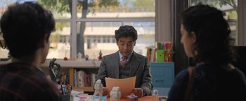 Movie still from “Anonymously Yours” (2021), directed by Maria Torres – A man sitting at a table reading a piece of paper; Medium shot, Over the shoulder angle