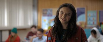 Movie still from “Anonymously Yours” (2021), directed by Maria Torres – A young girl with long brown hair is smiling for the camera; Close Up shot, Over the shoulder angle