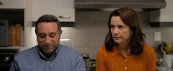 Movie still from “Anonymously Yours” (2021), directed by Maria Torres – A man and a woman in an orange shirt in a kitchen; Close Up shot, Over the shoulder angle
