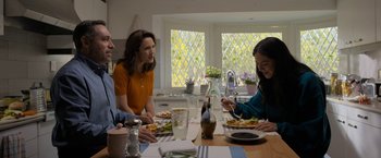 Movie still from “Anonymously Yours” (2021), directed by Maria Torres – Three people sitting at a table eating food; Medium shot, Over the shoulder angle