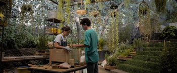 Movie still from “Anonymously Yours” (2021), directed by Maria Torres – A man and a woman working together in a plant shop; Wide shot, Low angle