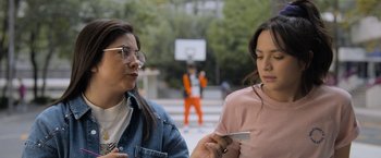 Movie still from “Anonymously Yours” (2021), directed by Maria Torres – Two young women are looking at a cell phone; Medium shot, Over the shoulder angle