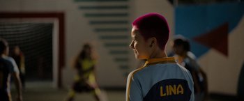 Movie still from “Anonymously Yours” (2021), directed by Maria Torres – A woman with pink hair is looking to her left; Close Up shot, Over the shoulder angle