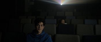 Movie still from “Anonymously Yours” (2021), directed by Maria Torres – A man sitting in front of a projector in a movie theater; Medium shot, Over the shoulder angle