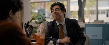 Movie still from “Anonymously Yours” (2021), directed by Maria Torres – A man sitting at a table with his eyes closed; Medium shot, Over the shoulder angle