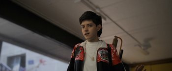 Movie still from “Anonymously Yours” (2021), directed by Maria Torres – A young man wearing a red and black jacket; Close Up shot, Low angle