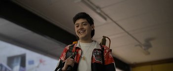 Movie still from “Anonymously Yours” (2021), directed by Maria Torres – A young man smiles while holding a microphone in his hand; Medium shot, Low angle