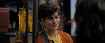 Movie still from “Anonymously Yours” (2021), directed by Maria Torres – A young man in an orange sweater is smiling for the camera; Close Up shot, Over the shoulder angle