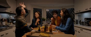 Movie still from “Anonymously Yours” (2021), directed by Maria Torres – A group of people sitting around a table eating pizza; Medium shot, Over the shoulder angle