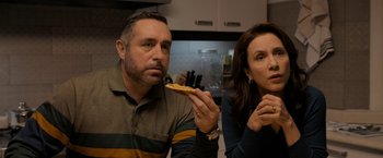 Movie still from “Anonymously Yours” (2021), directed by Maria Torres – A man and a woman sitting in a kitchen eating a piece of pizza; Medium shot, Over the shoulder angle
