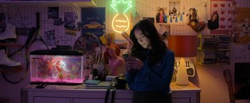 Movie still from “Anonymously Yours” (2021), directed by Maria Torres – A woman is looking at her cell phone in front of a neon sign; Medium shot, High angle