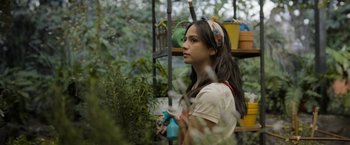 Movie still from “Anonymously Yours” (2021), directed by Maria Torres – A woman holding a spray bottle in a garden; Medium shot, Low angle