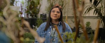 Movie still from “Anonymously Yours” (2021), directed by Maria Torres – A woman in a jean jacket and a headband; Close Up shot, Over the shoulder angle