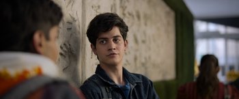 Movie still from “Anonymously Yours” (2021), directed by Maria Torres – A young man is standing in front of a stone wall; Close Up shot, Over the shoulder angle