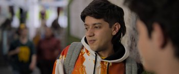 Movie still from “Anonymously Yours” (2021), directed by Maria Torres – A young man wearing a hooded sweatshirt and a backpack; Close Up shot, Over the shoulder angle