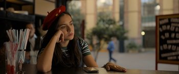 Movie still from “Anonymously Yours” (2021), directed by Maria Torres – A woman sitting at a table with a cell phone in her hand; Close Up shot, Low angle