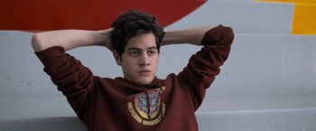 Movie still from “Anonymously Yours” (2021), directed by Maria Torres – A young man in a maroon hoodie is holding his hands behind his head; Close Up shot, Over the shoulder angle