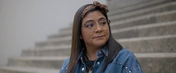 Movie still from “Anonymously Yours” (2021), directed by Maria Torres – A woman wearing glasses and a bow headband; Close Up shot, Over the shoulder angle