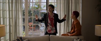 Movie still from “Anonymously Yours” (2021), directed by Maria Torres – A man standing in front of a window with his arms outstreched; Medium shot, Over the shoulder angle