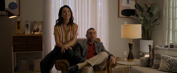 Movie still from “Anonymously Yours” (2021), directed by Maria Torres – A man and a woman sitting in a chair in front of a window; Medium shot, Low angle