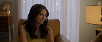 Movie still from “Anonymously Yours” (2021), directed by Maria Torres – A woman sitting in a chair smiling for the camera; Close Up shot, Over the shoulder angle