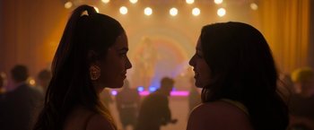 Movie still from “Anonymously Yours” (2021), directed by Maria Torres – Two young women standing next to each other in front of lights; Close Up shot, Over the shoulder angle