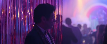 Movie still from “Anonymously Yours” (2021), directed by Maria Torres – A man wearing a suit and tie in a room; Medium shot, Over the shoulder angle