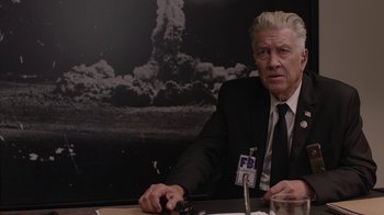 Movie still from “Twin Peaks” (2017), directed by David Lynch – A man sitting at a table in front of an fbi poster; Medium shot, Over the shoulder angle